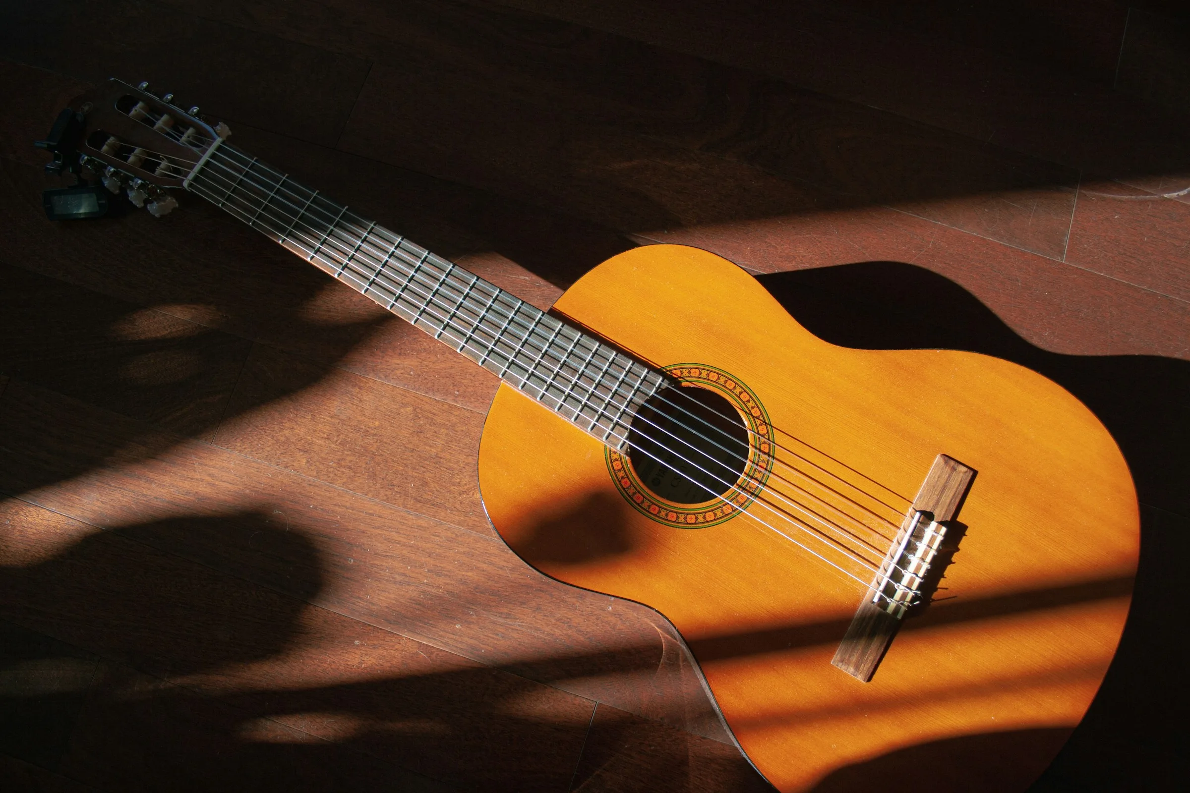 Placeholder de stock — guitarra clásica con luz dramática sobre suelo de madera, pendiente de foto real de Maison Guitars